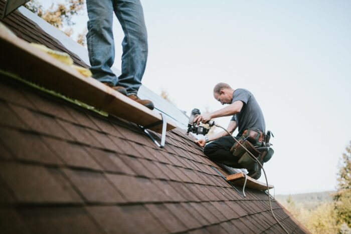 Roofing contractor using a nail gun to secure shingles on a residential roof, representing professional roofing services available through RoofMarketplace.